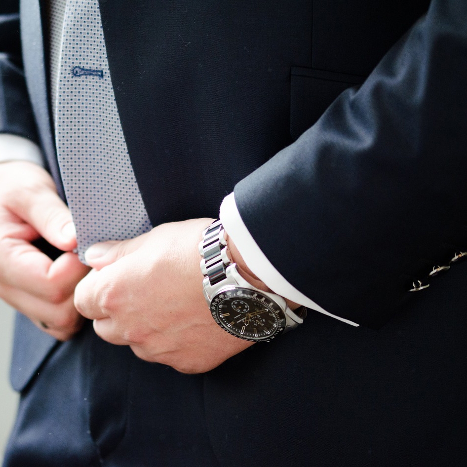 A person wearing a suit and wristwatch with a silver bracelet and black dial.
