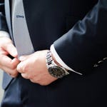A person wearing a suit and wristwatch with a silver bracelet and black dial.