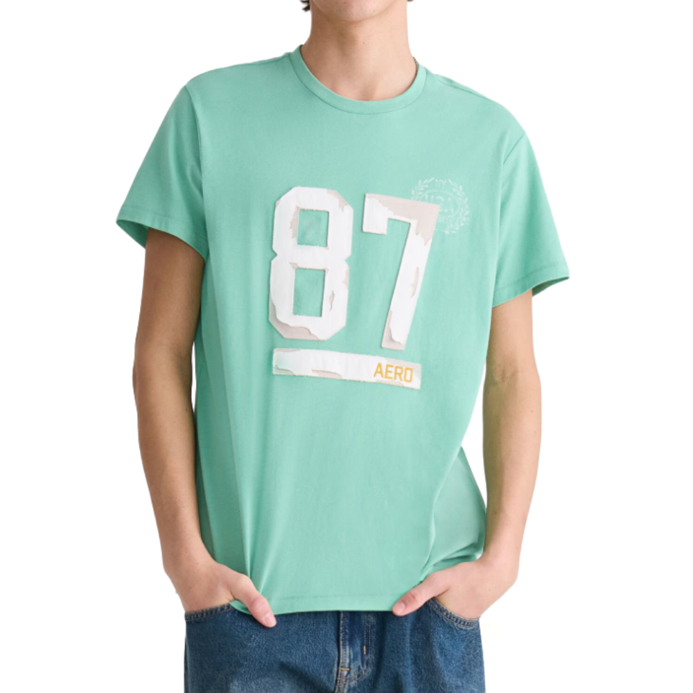A person wearing a mint green t-shirt with the number \“87\“ and the word \“AERO\“ printed on the front, paired with blue jeans.