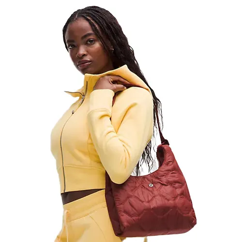 A person in a yellow tracksuit holds a red quilted shoulder bag with a small round detail.