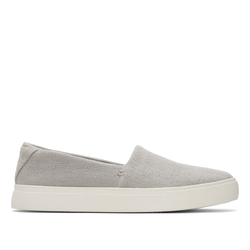 Kameron Slip On Sneaker features a minimalist design with a light gray textured fabric upper and a white rubber sole, offering a casual and comfortable look.