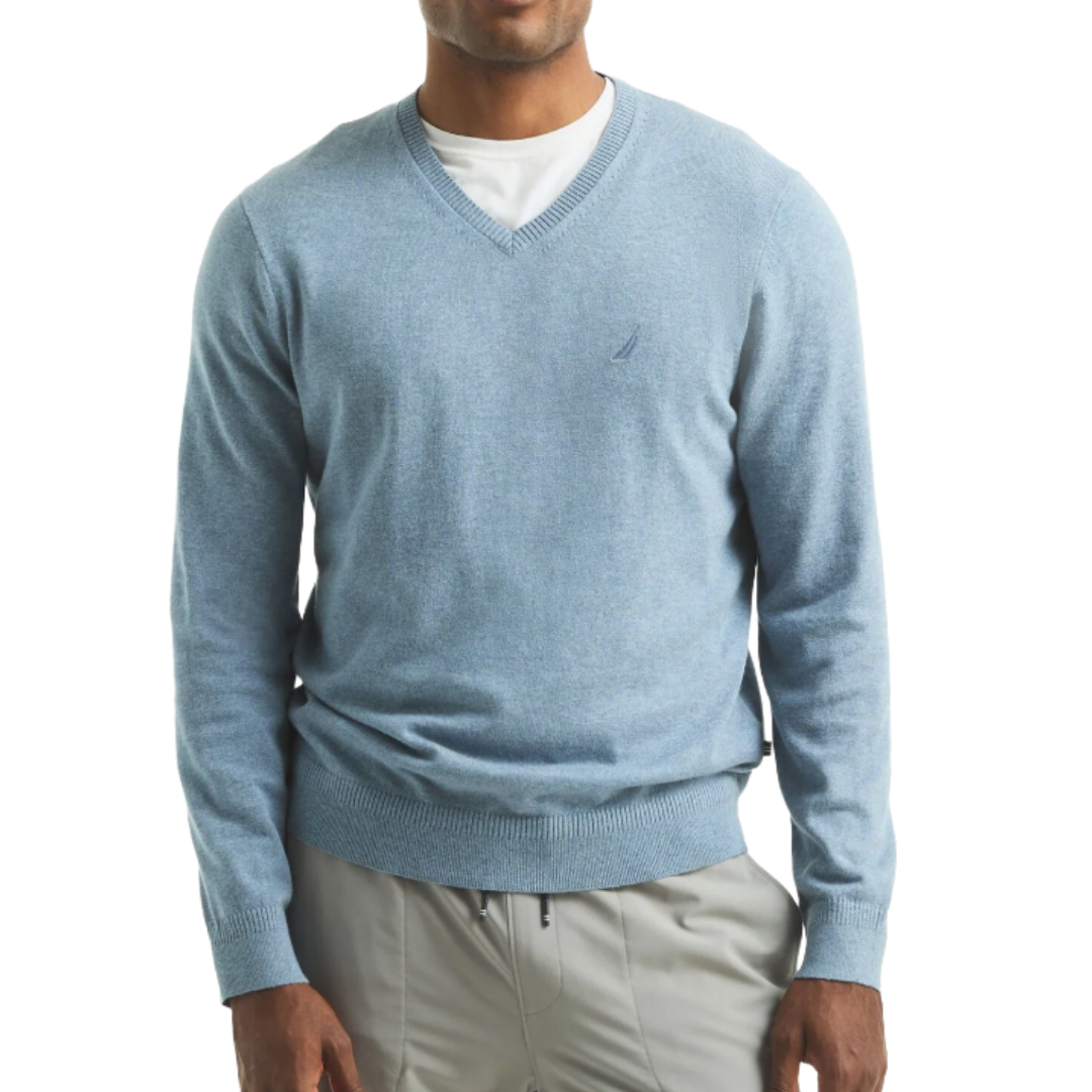 A man is wearing a light blue V-neck sweater over a white T-shirt, paired with light gray pants. The sweater has a small logo on the chest.