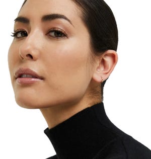 A small, minimalist 14K gold sleeper hoop earring is visible, offering a subtle and elegant touch to the ear. The design is simple and understated, suitable for daily wear.