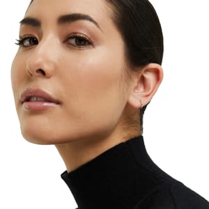 A small, minimalist 14K gold sleeper hoop earring is visible, offering a subtle and elegant touch to the ear. The design is simple and understated, suitable for daily wear.