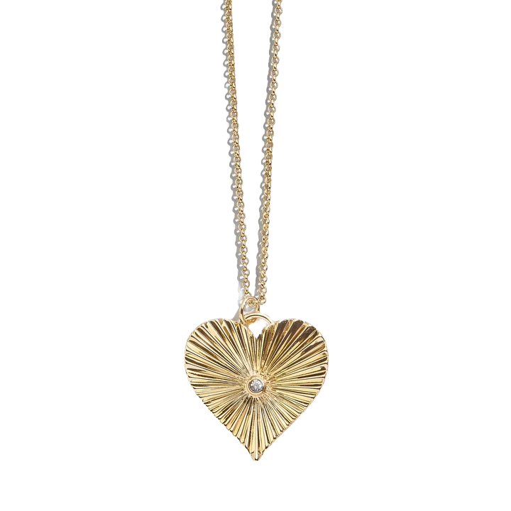 A gold heart-shaped pendant with a radiant, textured design and a small center gemstone, hanging from a delicate gold chain.