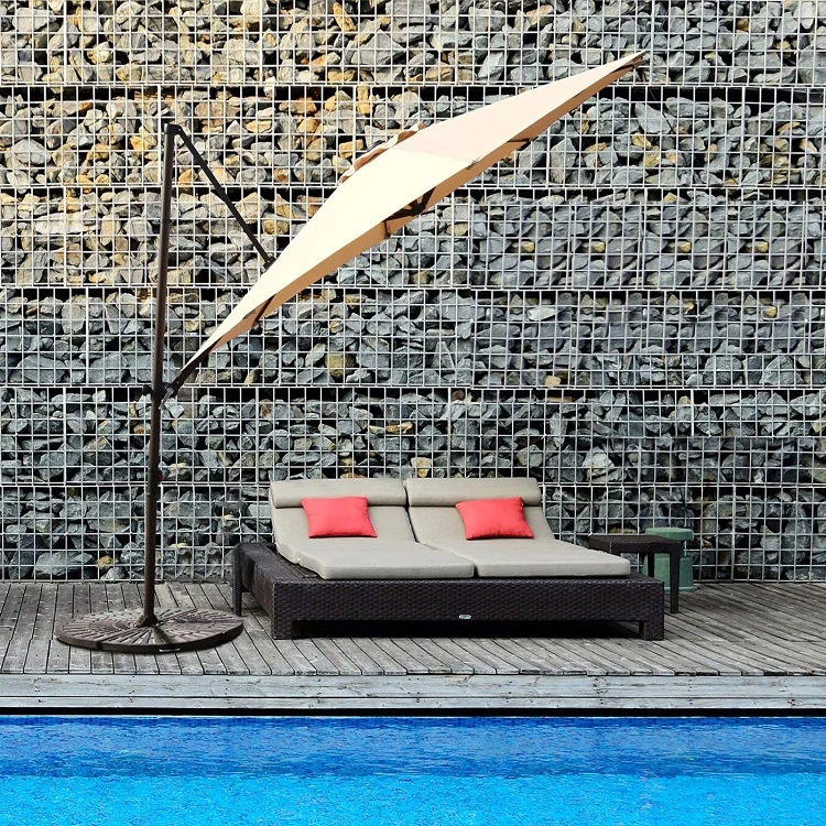 Outdoor lounge area with a double sunbed, red cushions, side table, and a cantilever umbrella near a pool.