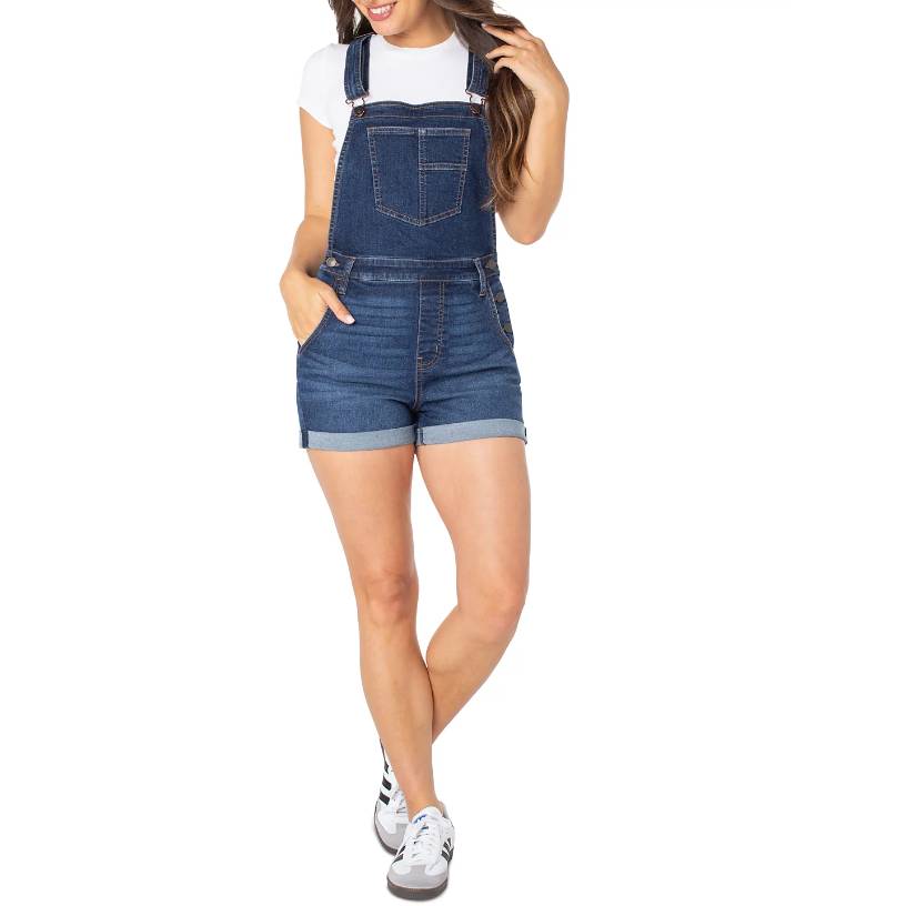 A woman is wearing denim short overalls paired with a white t-shirt and white sneakers.