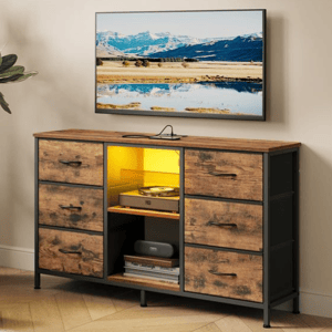 A woman holds a cup on a sofa next to a SONGMICS TV stand, designed to fit TVs up to 55 inches. The stand features drawers, a shelf with a yellow light, and various items like a record player and books.