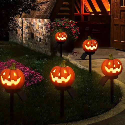 Halloween-themed pathway lights resembling carved pumpkins illuminate a walkway and garden area at night.