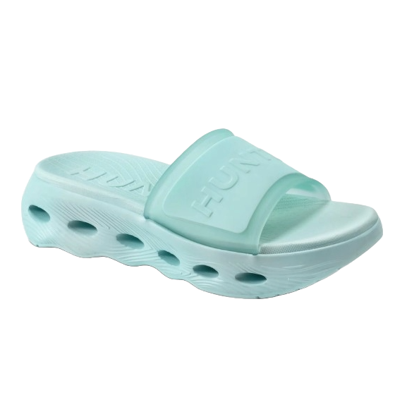 A light blue foam slide sandal with a thick sole featuring circular cutout patterns and a wide strap embossed with text.