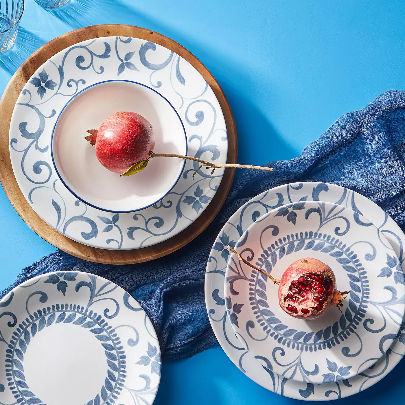 12pc Corelle Dinnerware set featuring plates with elegant blue floral and vine patterns on a white background, accompanied by wooden chargers and a decorative blue cloth. Includes a mix of dinner and side plates.