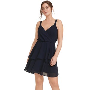 A woman wearing a navy, V-neck, tiered dress with spaghetti straps and a layered skirt.