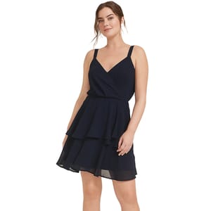 A woman wearing a navy, V-neck, tiered dress with spaghetti straps and a layered skirt.