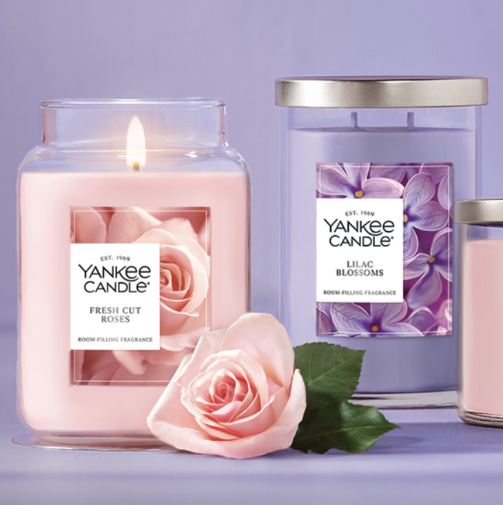 Yankee Candle collection with scents \“Fresh Cut Roses\“ and \“Lilac Blossoms\“ in various jar sizes alongside a pink rose.