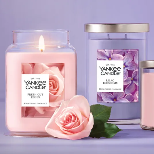 Yankee Candle collection with scents \“Fresh Cut Roses\“ and \“Lilac Blossoms\“ in various jar sizes alongside a pink rose.