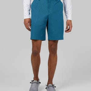 A man wearing teal shorts, a white long-sleeved shirt, and gray slip-on shoes.