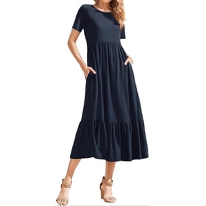 A navy blue short-sleeve midi dress features a loose fit with an empire waist and tiered skirt. It includes pockets on each side and is paired with braided heeled sandals.