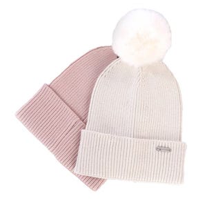 The 2pc Steve Madden Beanie Set includes a light pink ribbed beanie and a cream ribbed beanie with a white pom-pom on top. Both beanies have a cuffed design for added style and warmth.