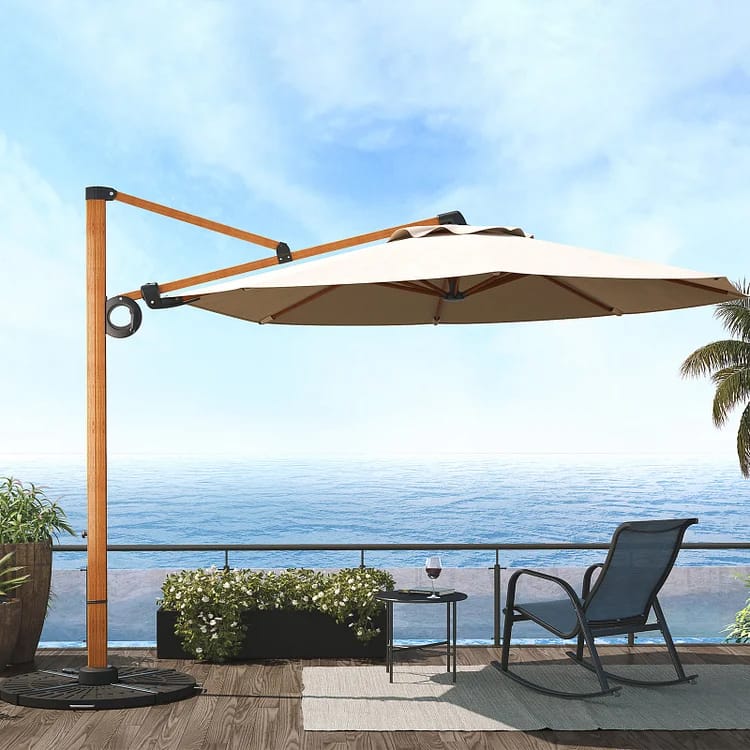 A beige cantilever patio umbrella, a lounge chair, and a small round table with a wine glass on it, next to a seaside balcony.