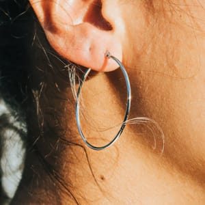A close-up shows a person wearing a large silver hoop earring on their left ear, with some strands of hair visible.