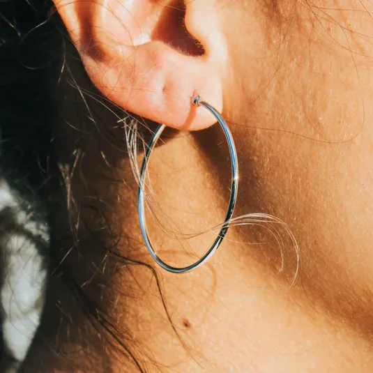 A close-up shows a person wearing a large silver hoop earring on their left ear, with some strands of hair visible.