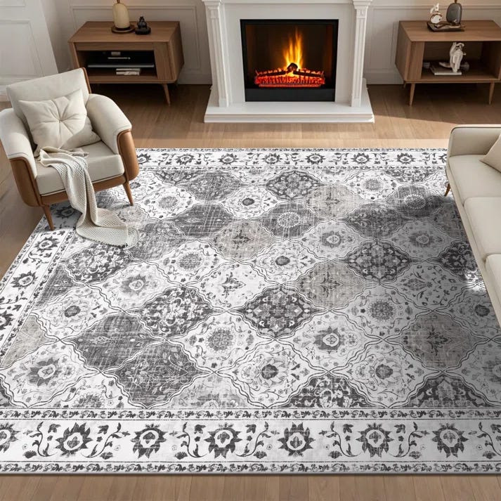 A living room features a patterned area rug with a floral and geometric design, placed between two armchairs and a sofa, in front of a lit fireplace.