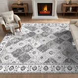 A living room features a patterned area rug with a floral and geometric design, placed between two armchairs and a sofa, in front of a lit fireplace.