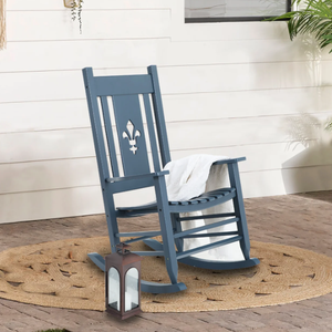 A blue wooden rocking chair with a fleur-de-lis cutout on the backrest is placed on a round woven rug, accompanied by a white lantern at its side.