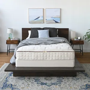 Bedroom setup with a dark wood platform bed, quilted mattress, gray bedding, and pillows. Two paintings hang above, flanked by modern nightstands with lamps and decor. A patterned rug completes the look.