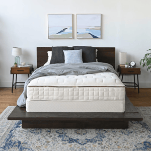Bedroom setup with a dark wood platform bed, quilted mattress, gray bedding, and pillows. Two paintings hang above, flanked by modern nightstands with lamps and decor. A patterned rug completes the look.