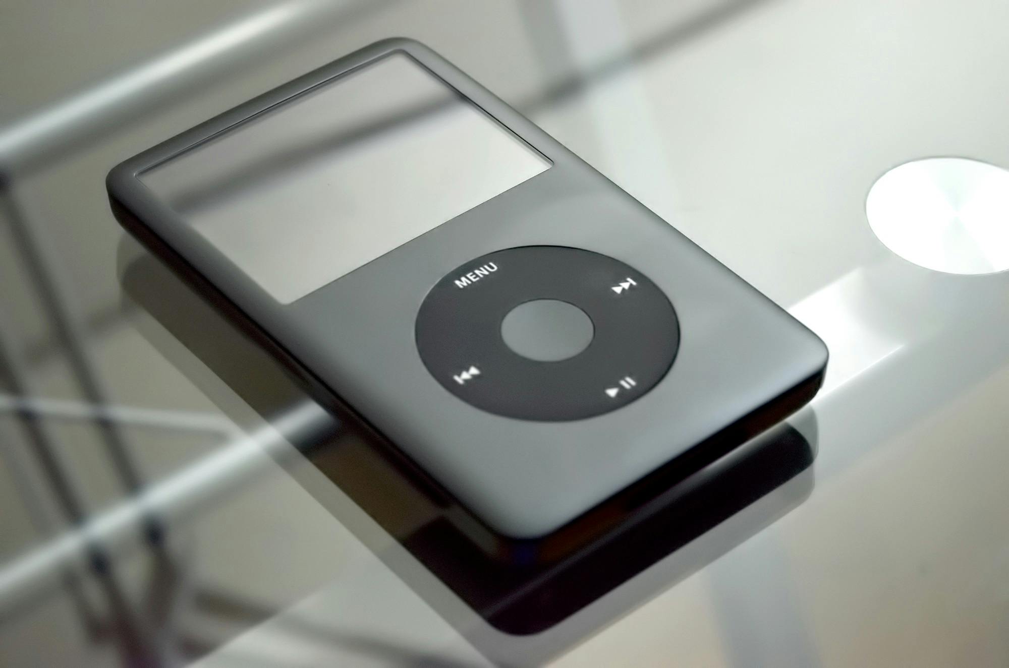 An iPod Classic with a click wheel interface, displayed on a reflective surface.