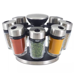 Rotating spice rack with stainless steel lids, containing eight glass jars labeled with spices like ground paprika, parsley, and turmeric, set on a sleek black and silver base for organized and accessible storage.