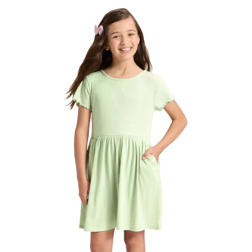 A young girl is wearing a light green, short-sleeved dress with a gathered waist and a pocket. She has a pink hair clip in her wavy brown hair.