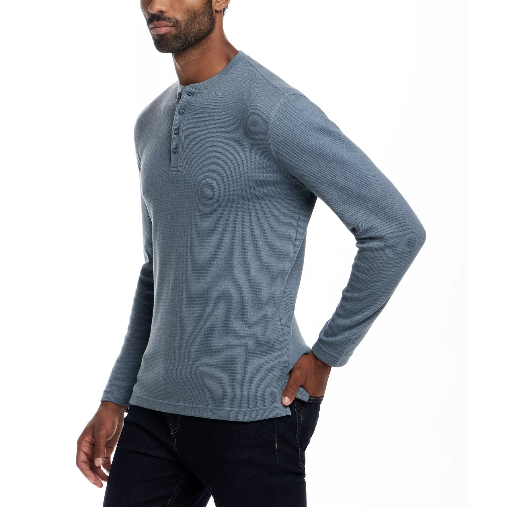 A man is wearing a blue long-sleeve henley shirt with a buttoned neckline and dark jeans.