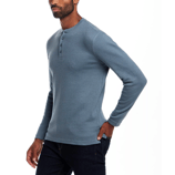 A man is wearing a blue long-sleeve henley shirt with a buttoned neckline and dark jeans.