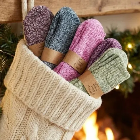 A cream knit stocking hangs by a fireplace, filled with four pairs of colorful socks in black, pink, purple, and green hues, each wrapped with brown paper bands.