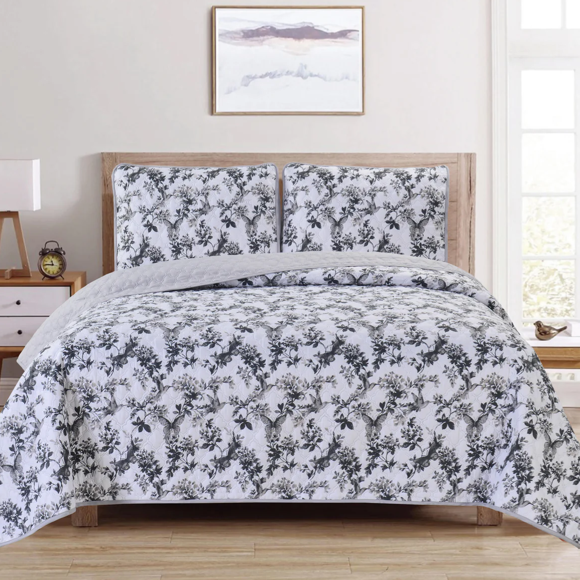 A bed set featuring a floral-patterned quilt and matching pillow shams; includes a wooden headboard, a nightstand with a lamp, an alarm clock, and a small decorative sculpture.