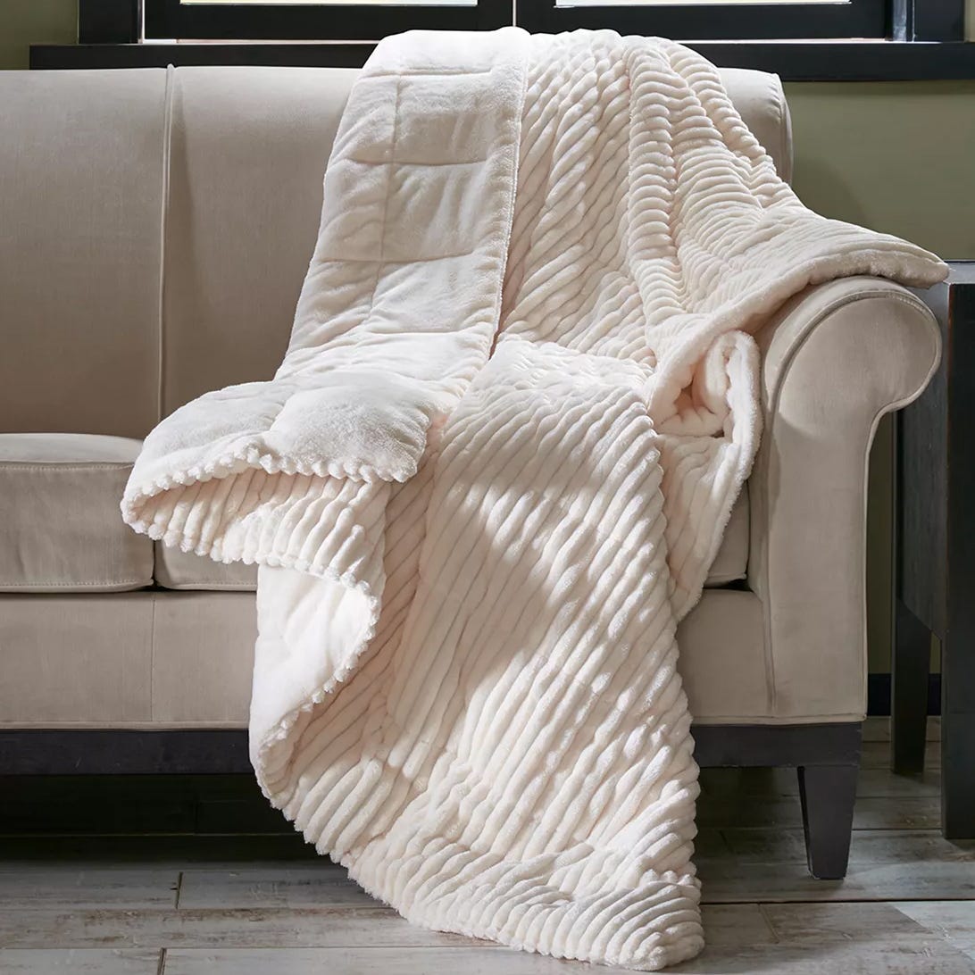 A plush, cream-colored throw blanket with a textured, ribbed pattern draped over a beige sofa.