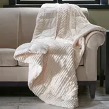 A plush, cream-colored throw blanket with a textured, ribbed pattern draped over a beige sofa.
