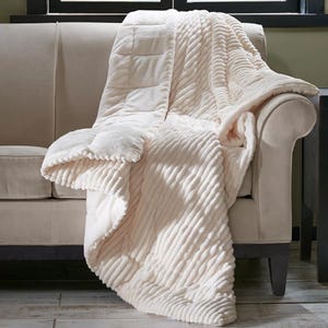 A plush, cream-colored throw blanket with a textured, ribbed pattern draped over a beige sofa.