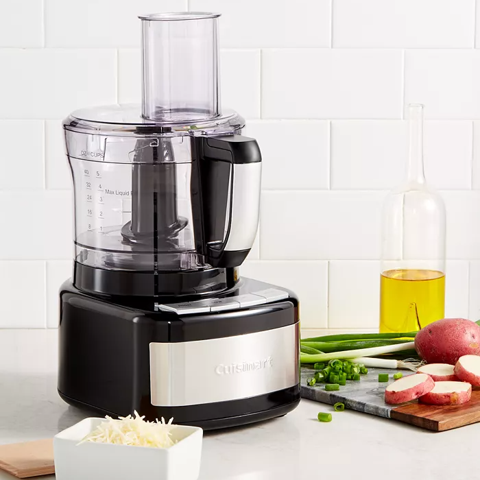 A Cuisinart food processor on a kitchen counter with chopped vegetables nearby.