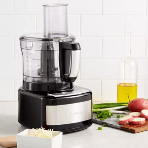 A Cuisinart food processor on a kitchen counter with chopped vegetables nearby.