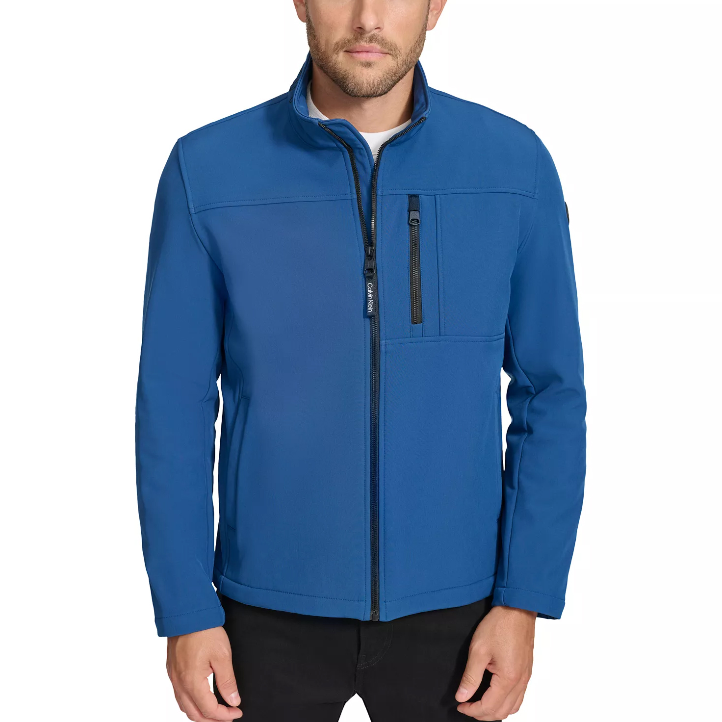 A man is wearing a blue zip-up softshell jacket with a high collar and a zippered chest pocket, paired with black pants.