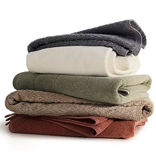 A stack of folded blankets in various earthy tones, including gray, cream, green, brown, and rust.