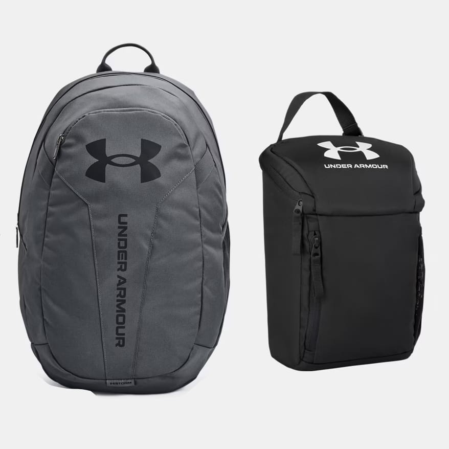 Two Under Armour backpacks: one gray with a prominent logo, and one black with a top handle and side pocket.