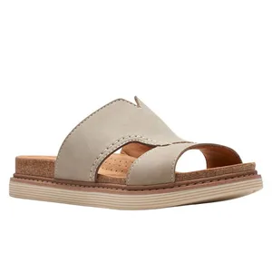 A beige slide sandal with an open-toe design, featuring a crisscross leather upper and a cork footbed for added comfort. The sole has a low, textured platform.