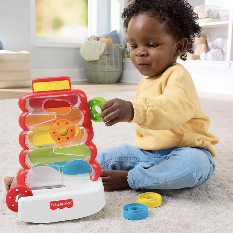 Child playing with Fisher-Price corn popper toy featuring colorful discs and a spiral track on a soft carpet indoors.