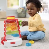 Child playing with Fisher-Price corn popper toy featuring colorful discs and a spiral track on a soft carpet indoors.