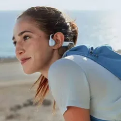 A person wearing bone conduction headphones by the sea, dressed in a light blue athletic outfit with a matching backpack.