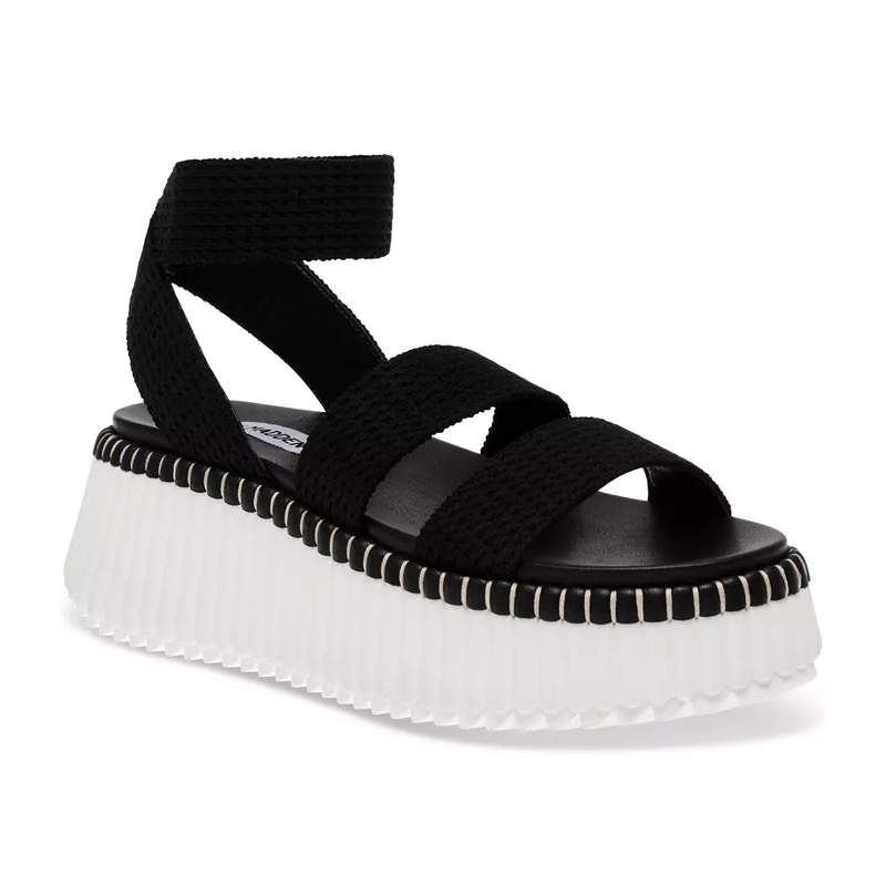 Black platform sandals with thick, stretchy straps, a chunky white sole edged with a black stitch-like detail, and an ankle strap fastening.